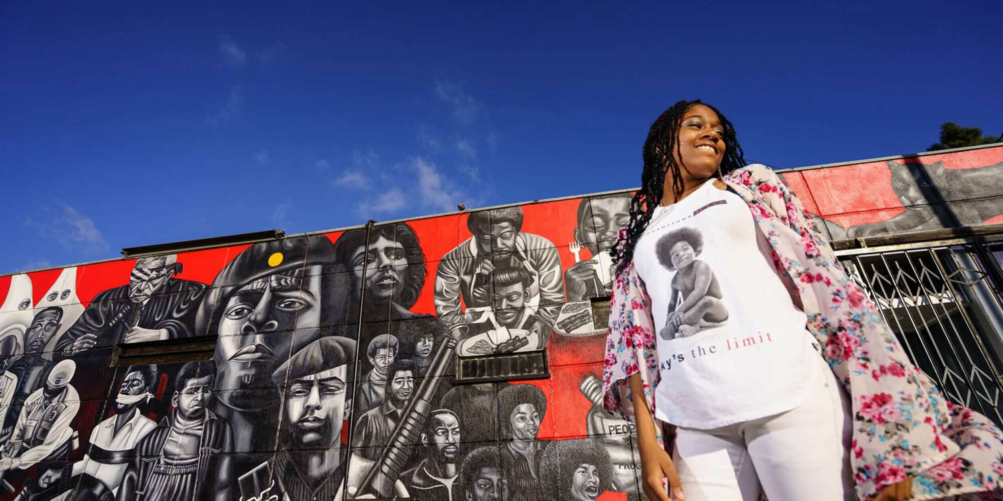 A women standing under a blue sky in front of a painted mural