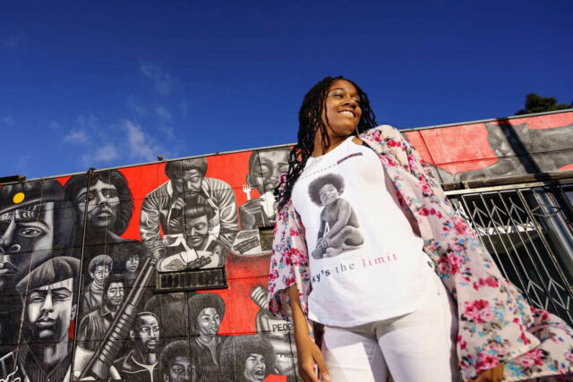 A women standing under a blue sky in front of a painted mural